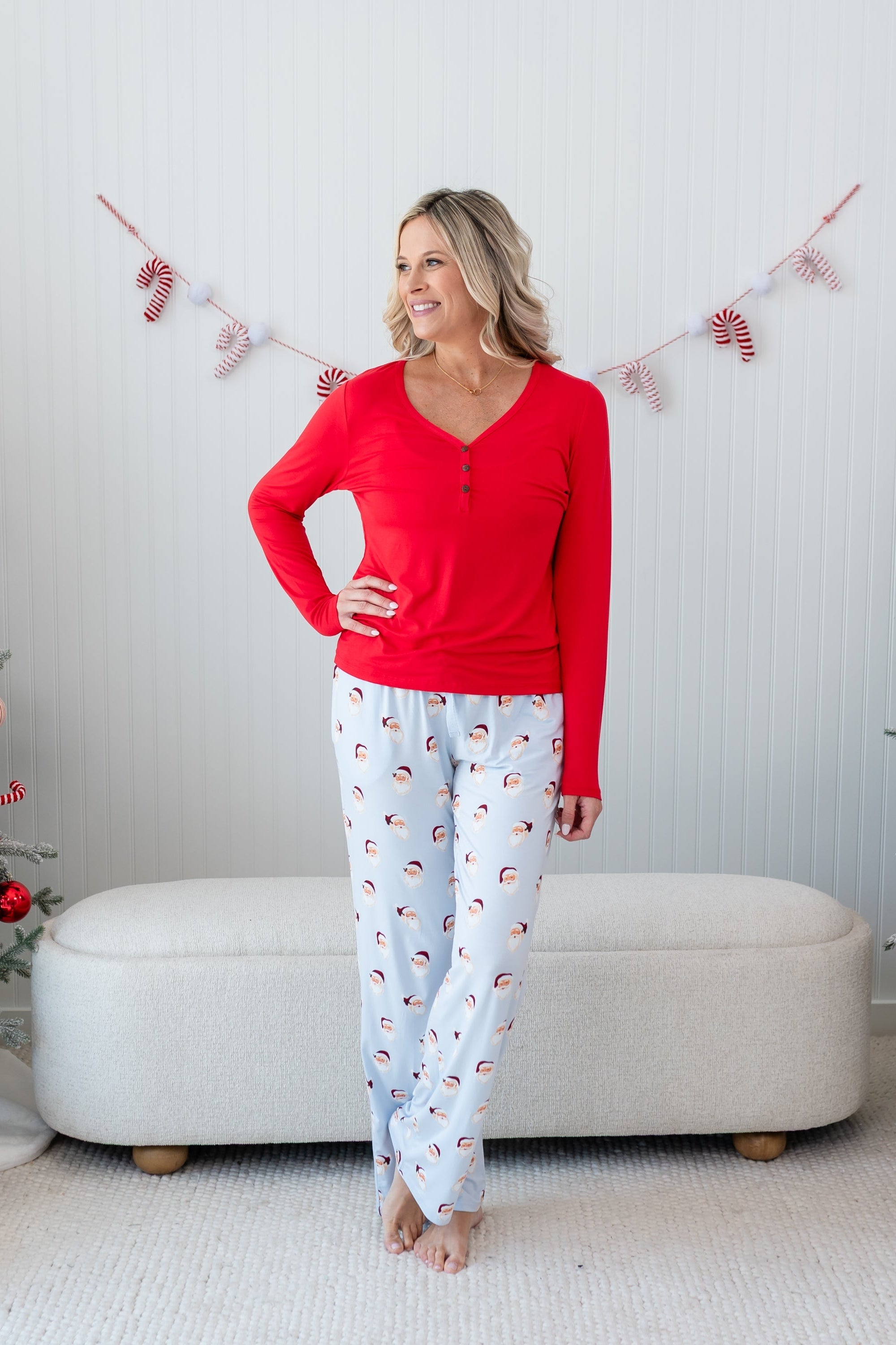 Female model standing in front of a cream colored ottoman wearing the Women's Lounge Pants in Vintage Santa with a cardinal women's henley