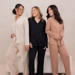 Three female models standing beside one another wearing the Long-Sleeved Women's Pajama Set in Latte with Latte Trim, Midnight with Midnight trim and Bisque with Bisque Trim