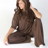 Model sitting with one knee up, looking downwards and wearing the Women's Short Sleeve Tee in Espresso with matching bottoms
