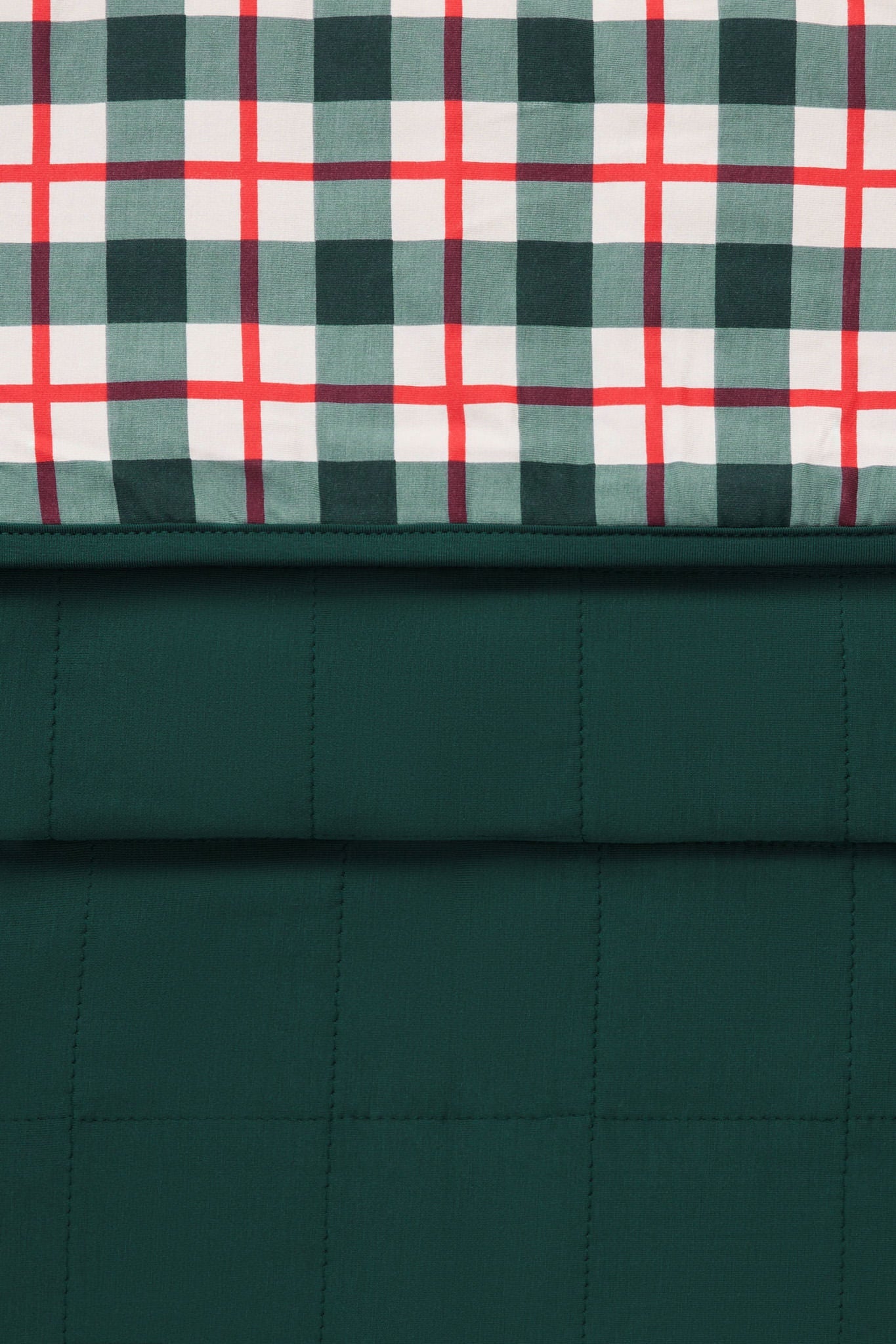 A close-up of a quilted fabric product showing two pattern sections: a dark green plaid top panel with white and red intersecting stripes, and a solid dark green quilted lower section.