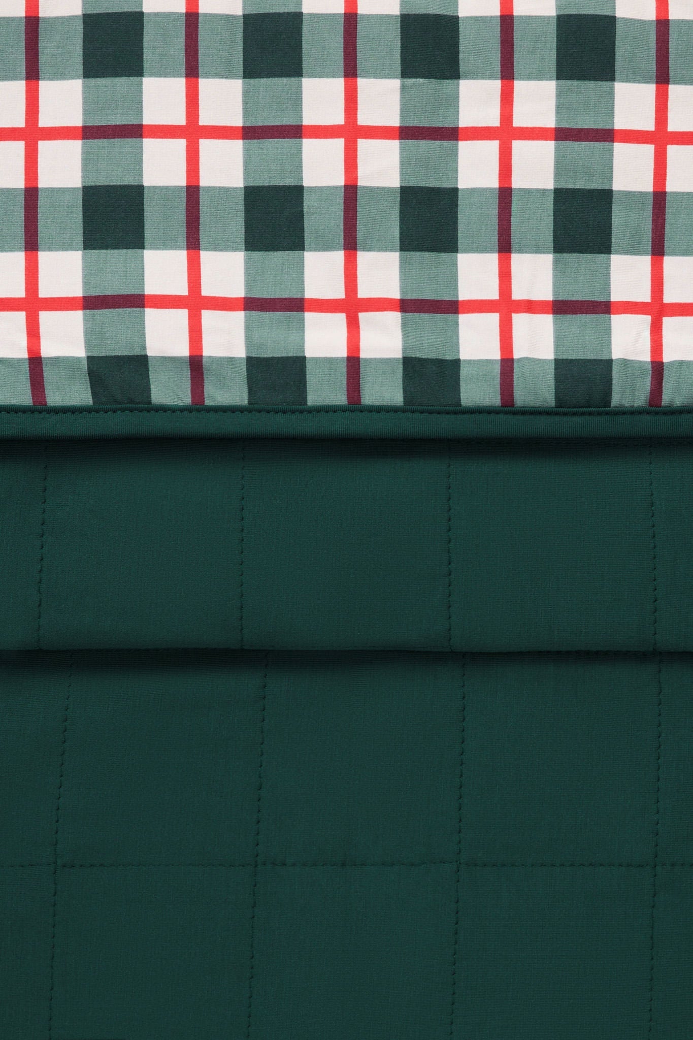 A close-up of a quilted fabric product showing two pattern sections: a dark green plaid top panel with white and red intersecting stripes, and a solid dark green quilted lower section.