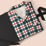 A folded plaid pajama shirt in green, white, and red is presented in a black gift box with a black ribbon on a light beige background.