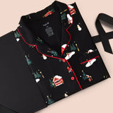 A black pajama set with a Christmas-themed print, featuring red piping and red buttons, presented on a black gift box with a ribbon against a light beige background.