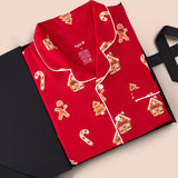 A red long-sleeve pajama shirt with white piping and gingerbread-themed prints, presented in an open black gift box on a light beige background.