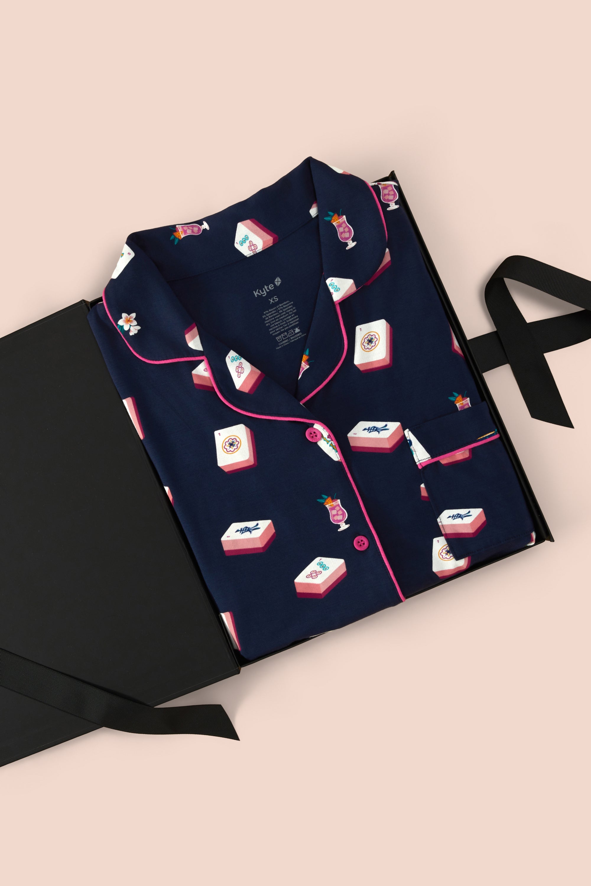 A navy blue pajama set with pink piping and a playful print of red, white, and blue mahjong tiles, presented in an open black gift box on a light pink background.