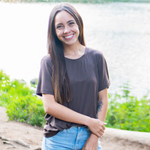 Smiling model standing by a lake wearing the Women's Crew Neck Tee in Espresso