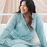 Woman wearing a light blue satin pajama set sitting on a bed with a neutral background