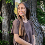 Woman smiling in front of a tree looking to the side while modeling the Women's Crew Neck Tee in Espresso