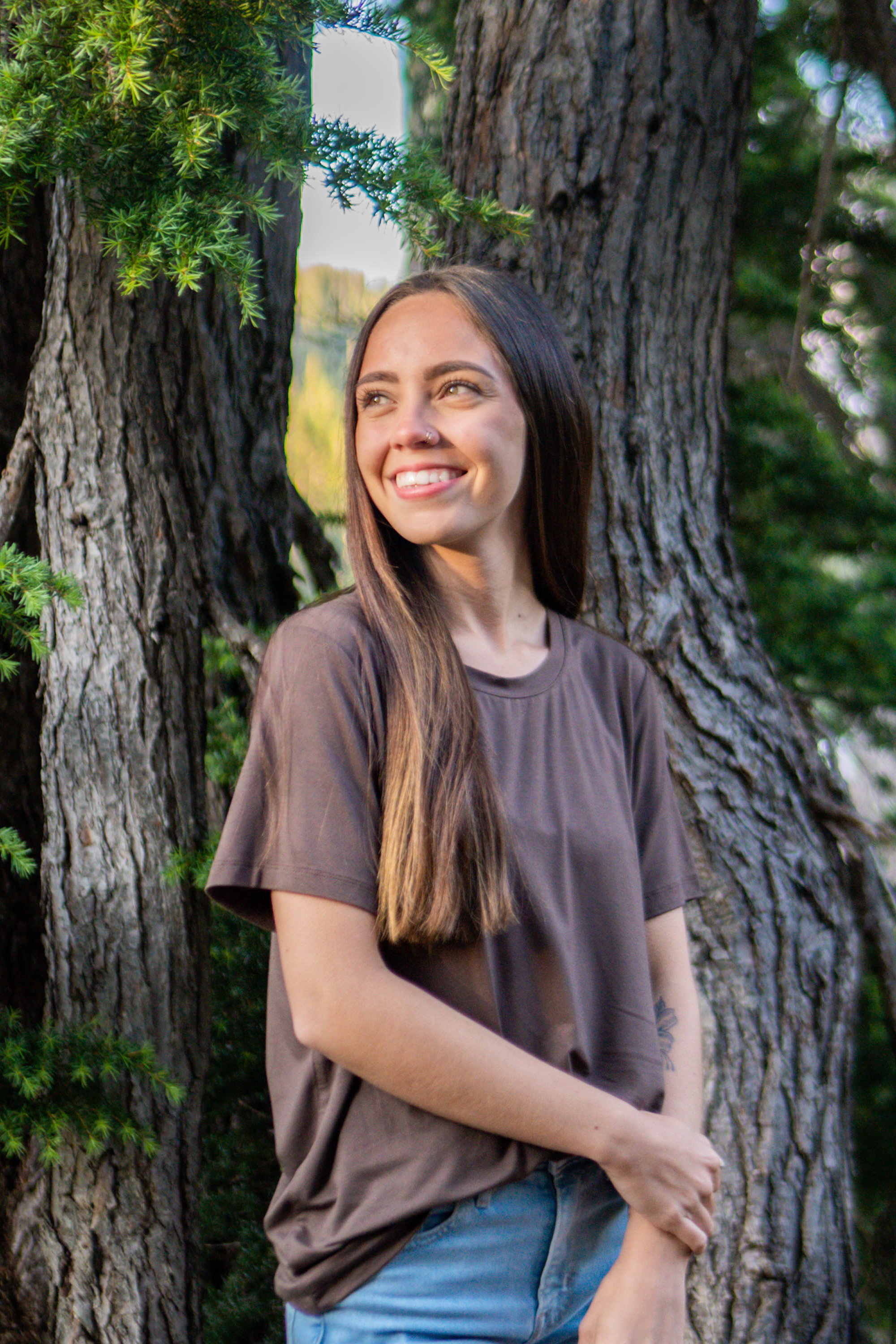 Woman smiling in front of a tree looking to the side while modeling the Women's Crew Neck Tee in Espresso
