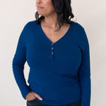 Model looking to the side while wearing the Women's Long Sleeve Henley Tee in Tahoe paired with dark denim jeans