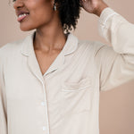 Woman wearing a beige button-up pajama shirt against a beige background