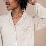 Woman wearing a beige button-up pajama shirt against a beige background
