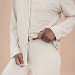 Person wearing a beige button-up pajama shirt and pants against a beige background