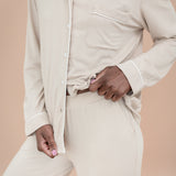 Person wearing a beige button-up pajama shirt and pants against a beige background