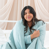 Woman wrapped in a light blue blanket against a beige curtain background