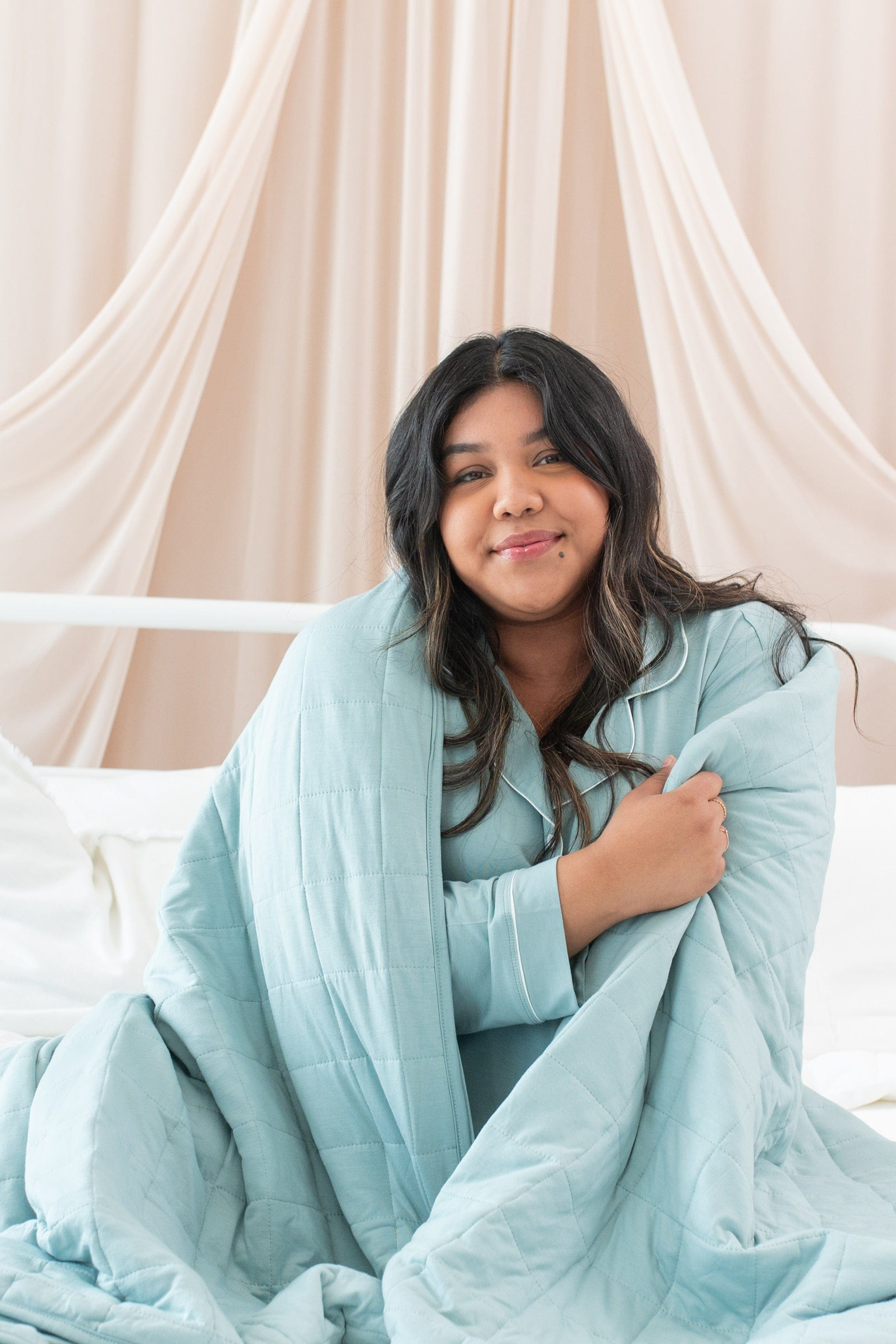 Woman wrapped in a light blue blanket against a beige curtain background