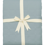 Light blue quilt with a white ribbon on a white background