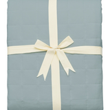 Light blue quilt with a white ribbon on a white background