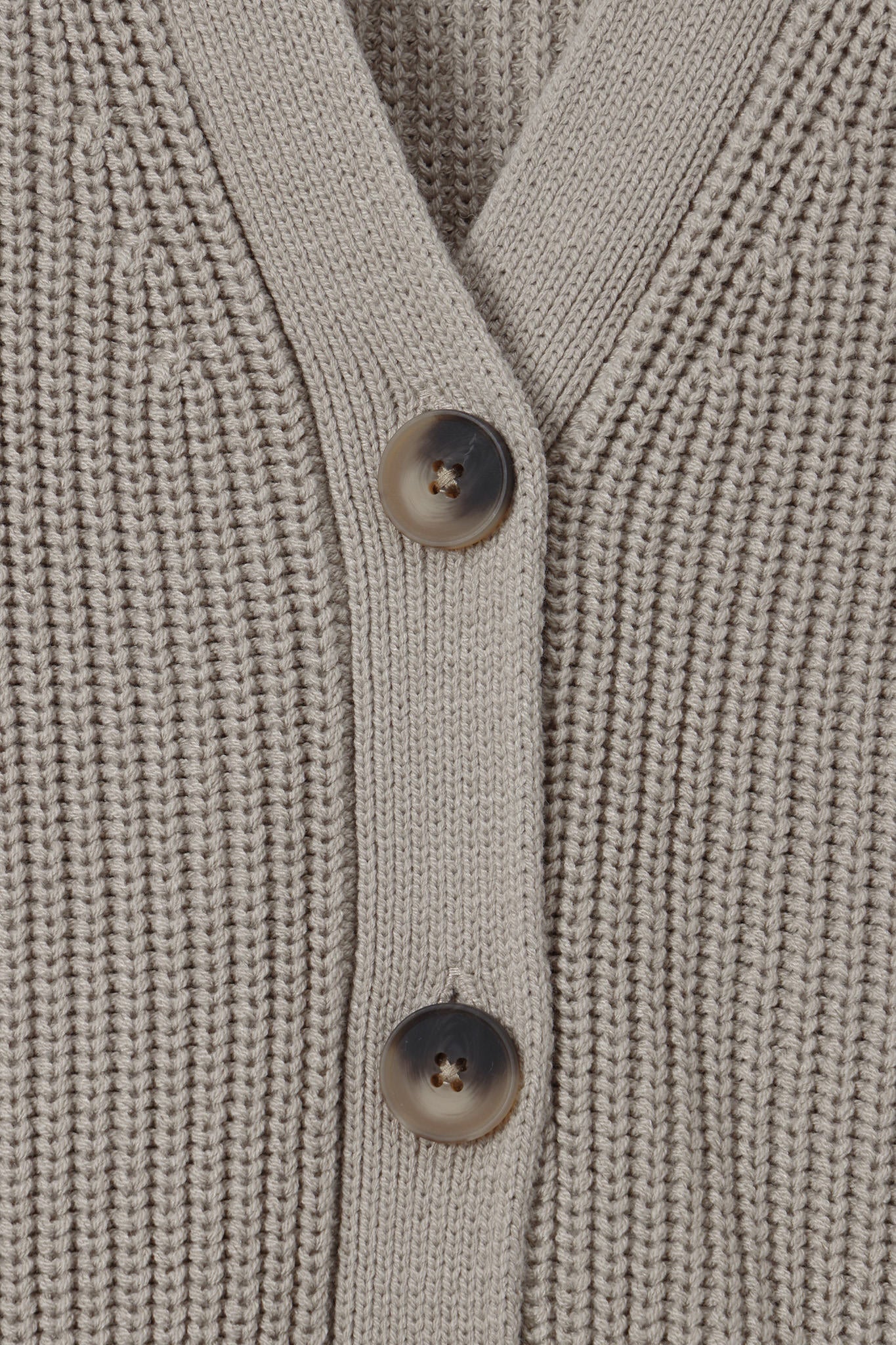 Close-up of a ribbed knit cardigan sweater in a light taupe-beige color, featuring two dark brown buttons on the front.