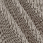 Close-up of a ribbed knit fabric in a warm taupe-beige color, showing the detailed texture and folds of the material.