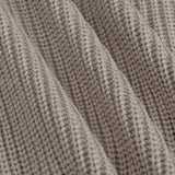 Close-up of a ribbed knit fabric in a warm taupe-beige color, showing the detailed texture and folds of the material.