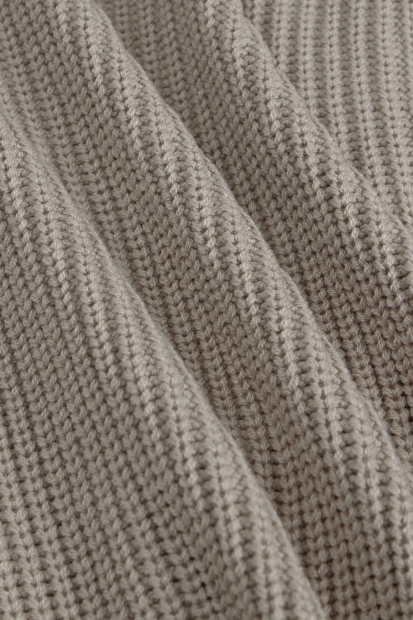 Close-up of a ribbed knit fabric in a warm taupe-beige color, showing the detailed texture and folds of the material.