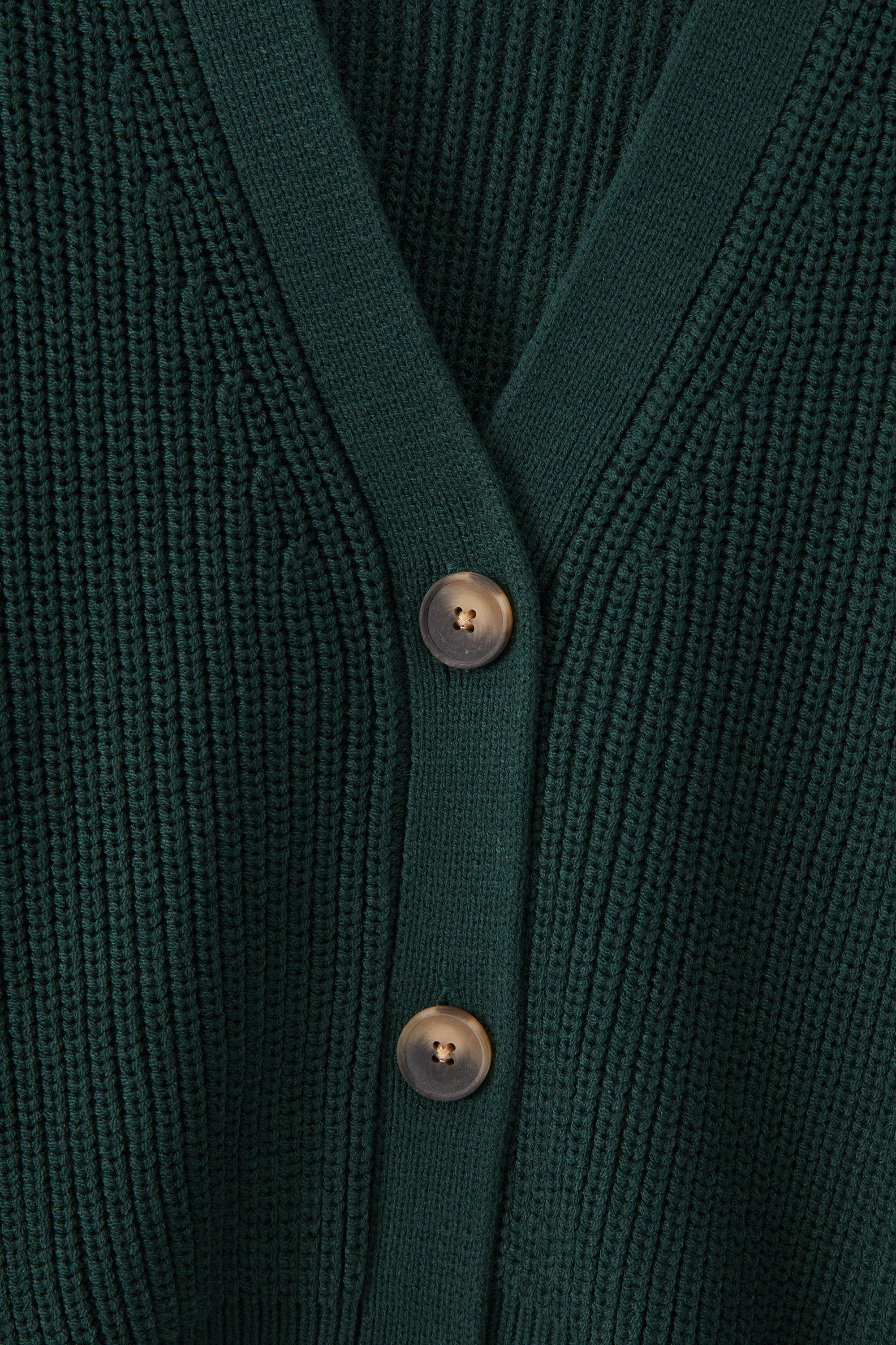 Close-up of a dark green ribbed knit cardigan with a V-neck and two metallic buttons.