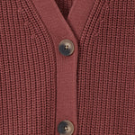 Close-up of a ribbed knit cardigan in a dusty rose or mauve pink color, featuring three dark gray buttons down the front center.