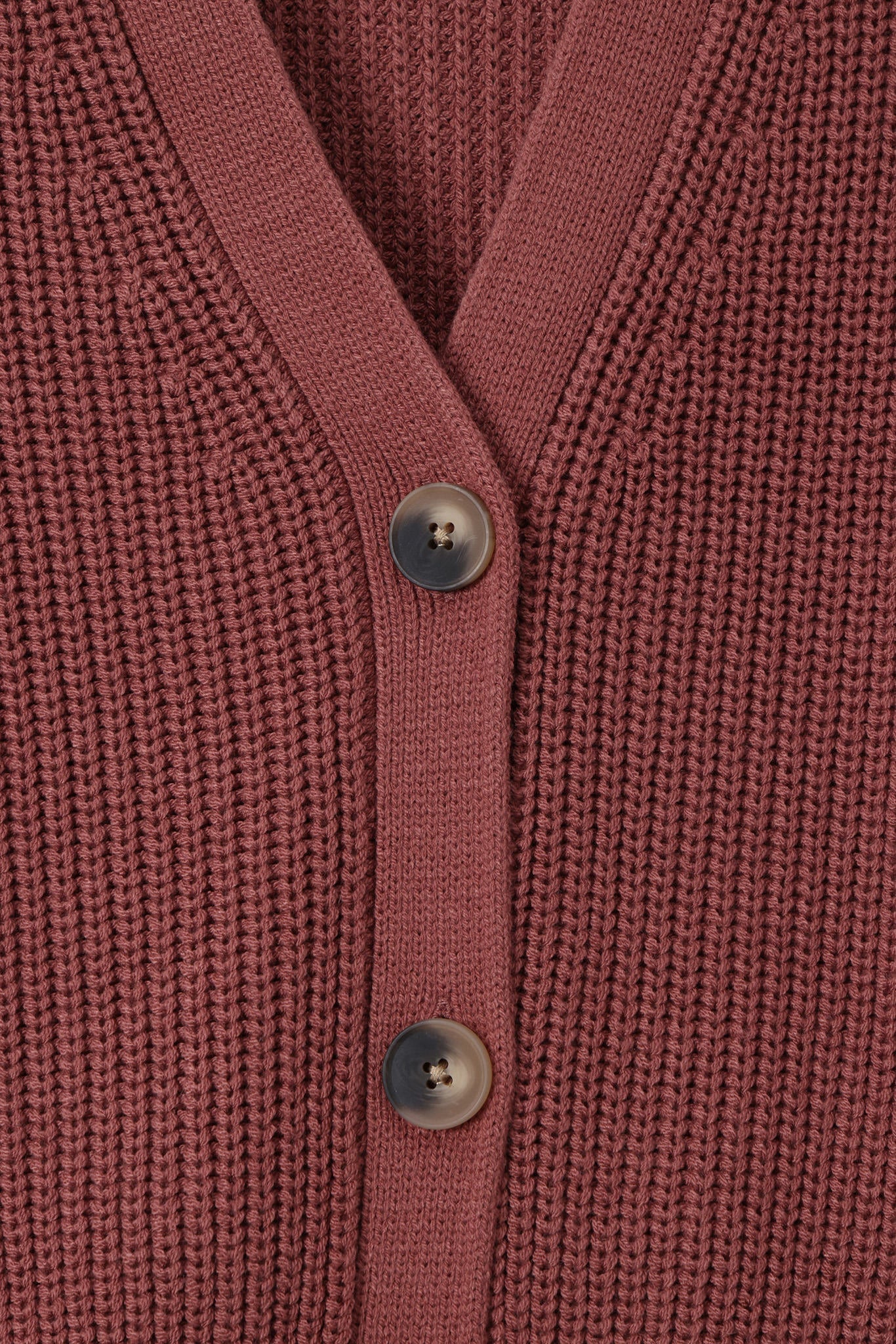 Close-up of a ribbed knit cardigan in a dusty rose or mauve pink color, featuring three dark gray buttons down the front center.