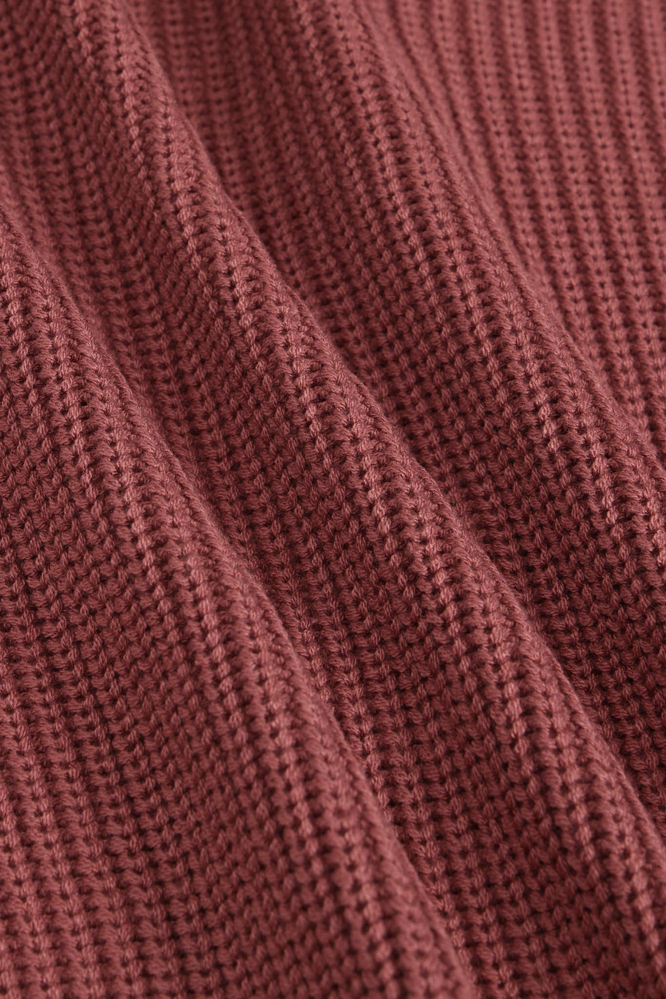 Close-up of a ribbed knit fabric in a dusty rose or mauve color, showing the detailed texture and folds of the material.