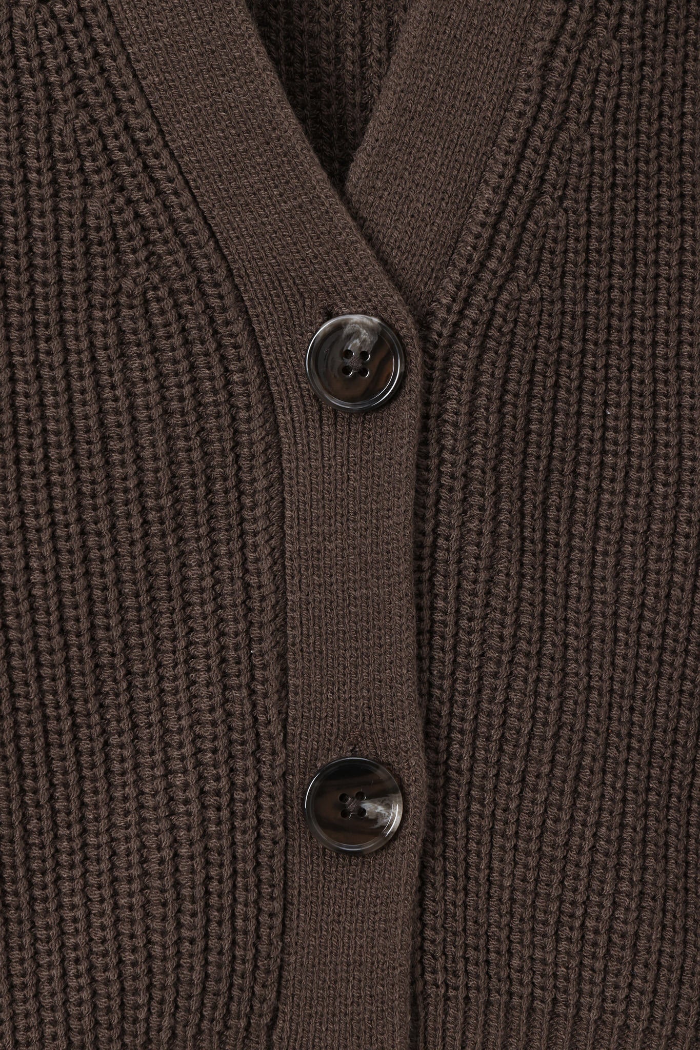 Close-up of a ribbed knit cardigan in dark brown with two dark buttons on a matching brown background.