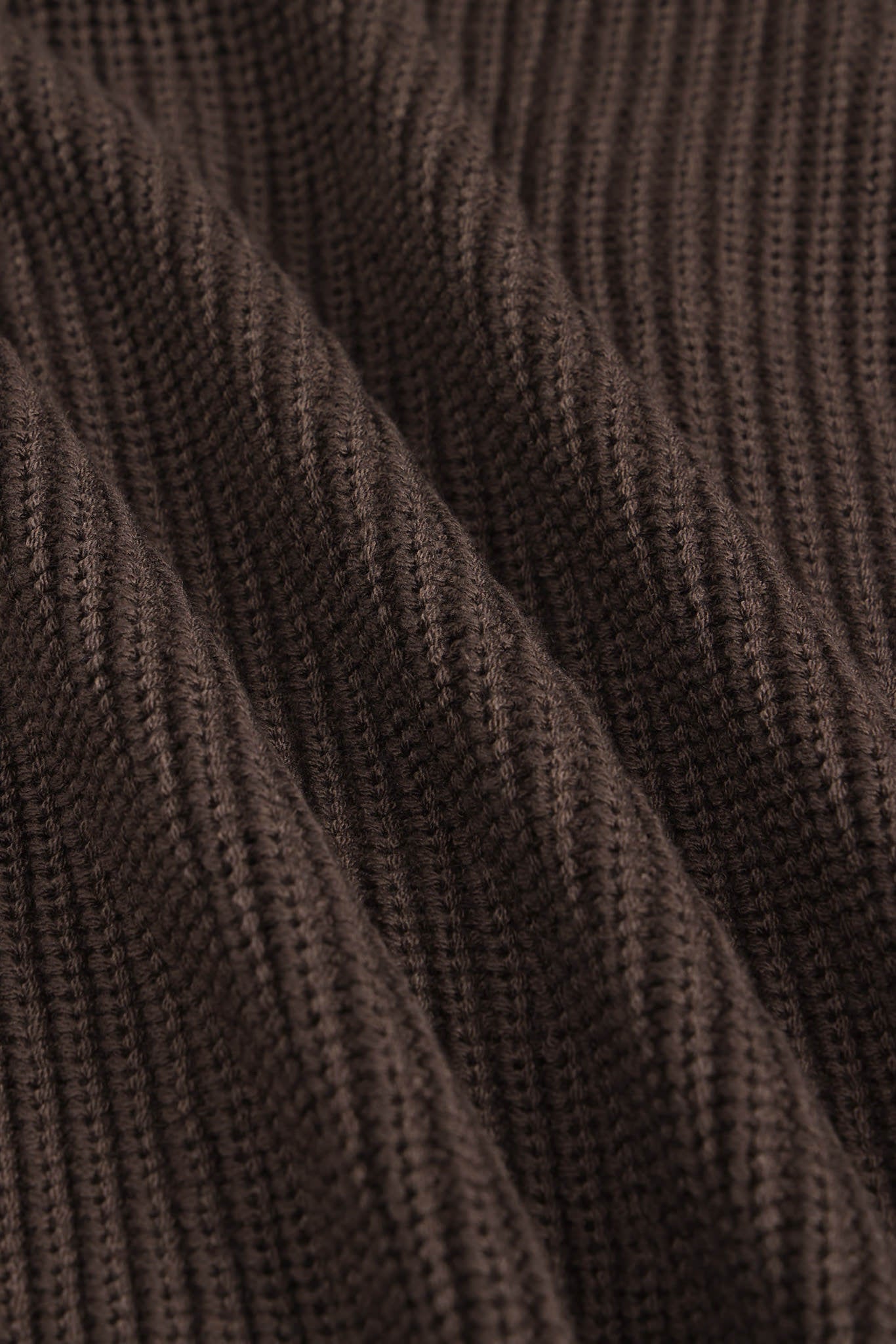 Close-up of a dark brown ribbed knit fabric texture with soft folds and a fine woven pattern.