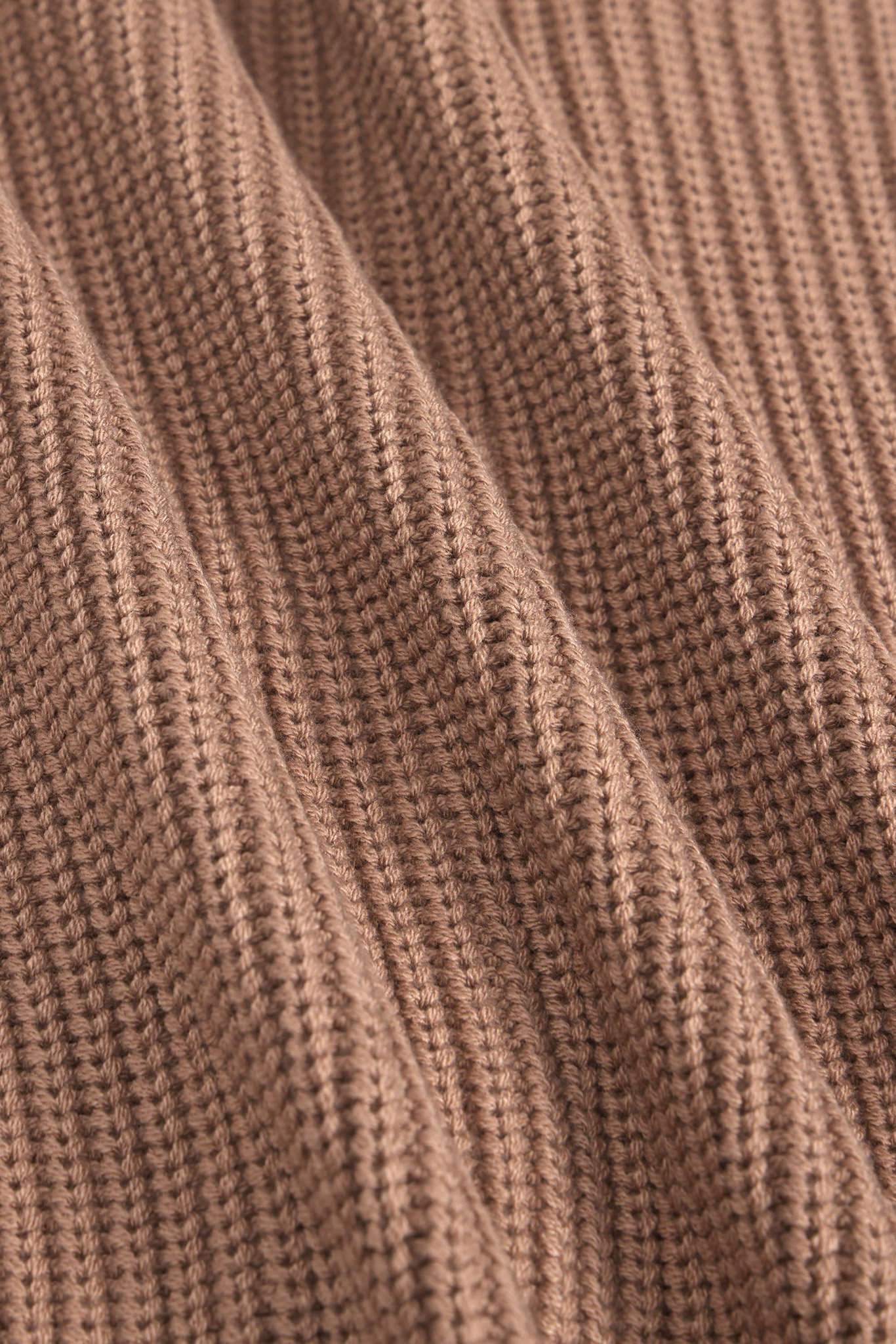 Close-up of a ribbed knit fabric in a warm taupe-brown color, showing the detailed texture and folds of the material.