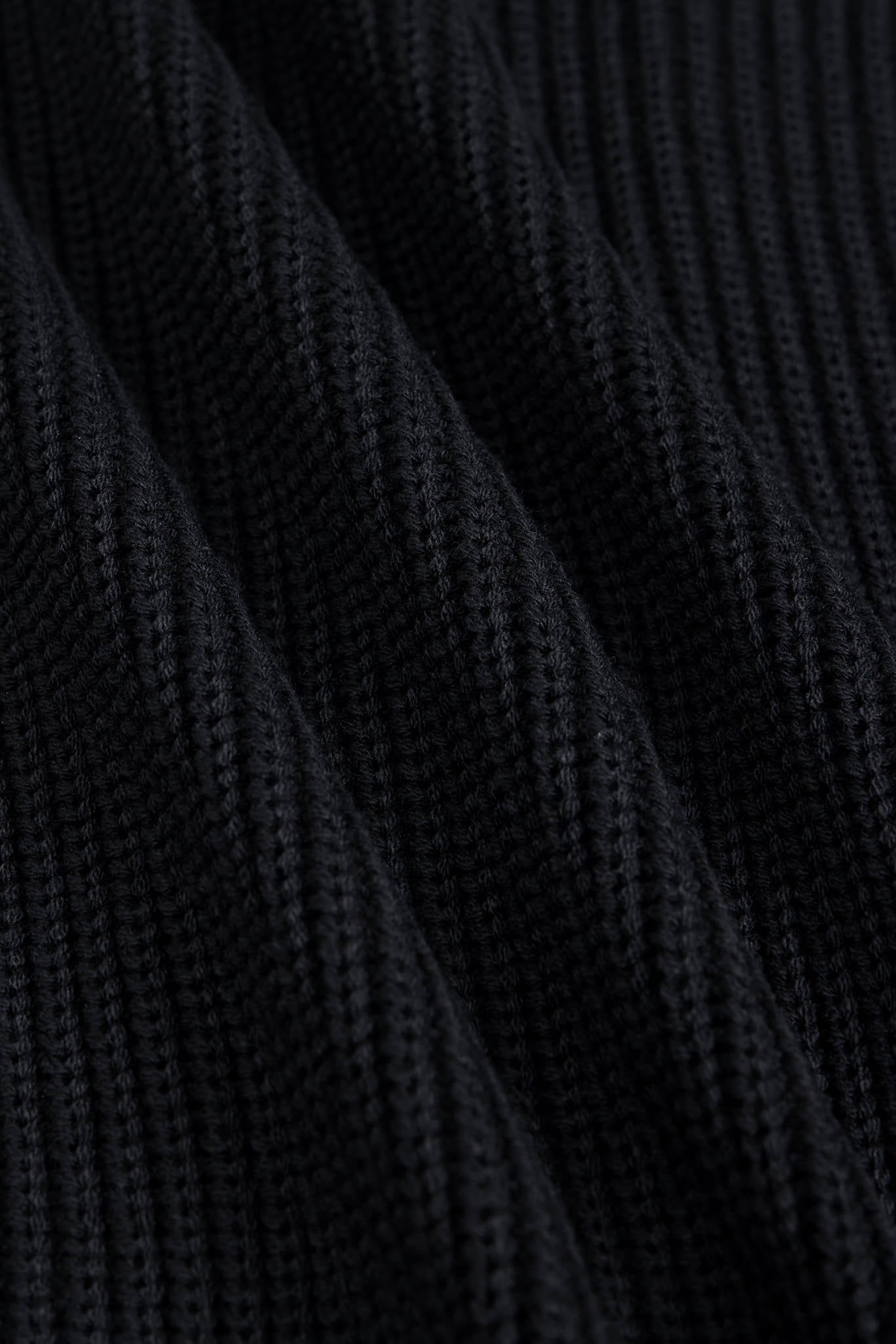 Close-up of a black ribbed knit fabric texture with soft diagonal folds.