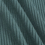 Close-up of a ribbed knit fabric in a muted blue-green color, showing the detailed texture and folds.