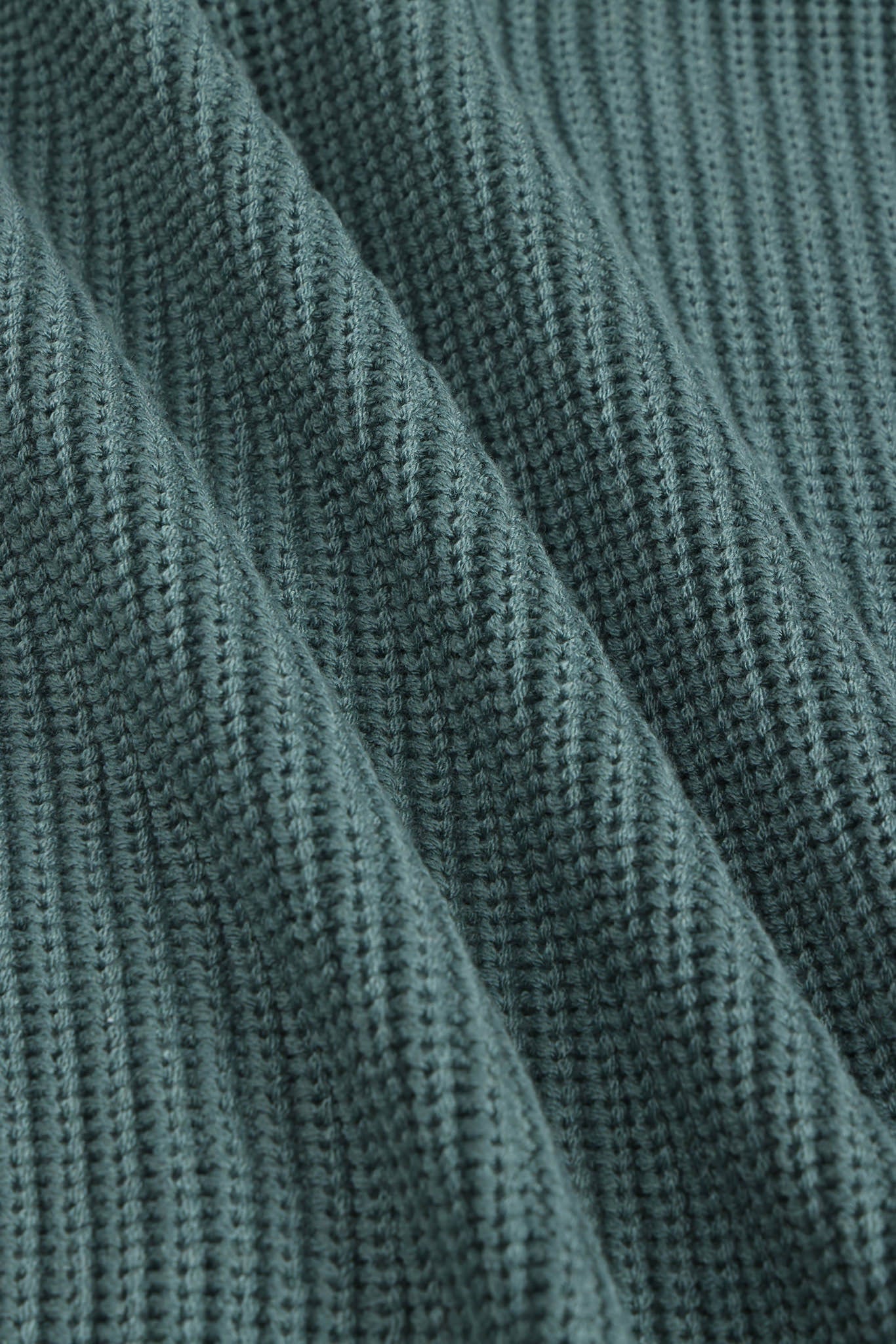 Close-up of a ribbed knit fabric in a muted blue-green color, showing the detailed texture and folds.
