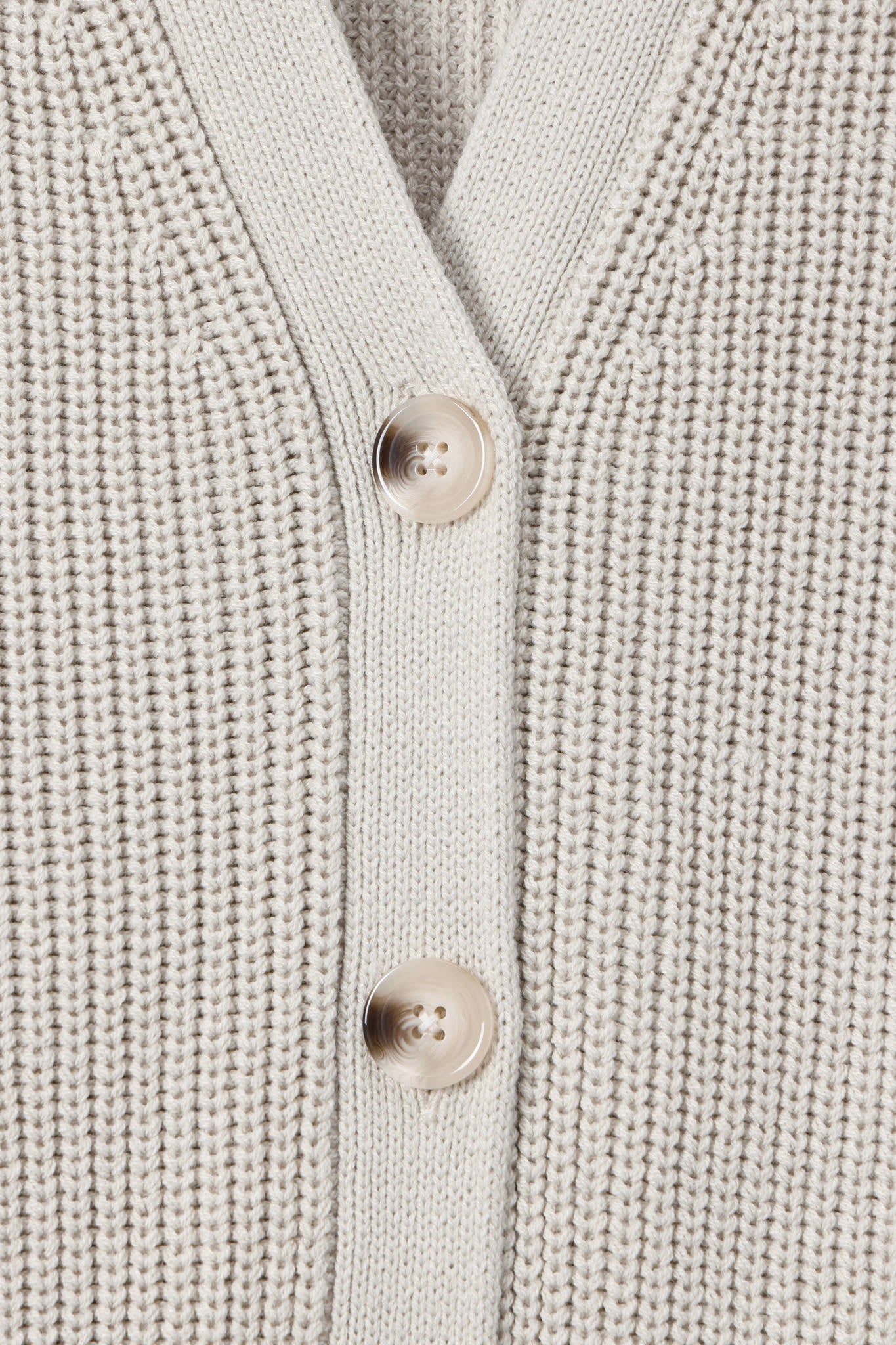 Close-up of a cream-colored ribbed knit cardigan sweater showing the button placket with two light beige buttons.