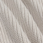 Close-up of a ribbed knit fabric in a light oatmeal beige color, showing the detailed texture and folds of the yarn.