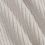 Close-up of a ribbed knit fabric in a light oatmeal beige color, showing the detailed texture and folds of the yarn.