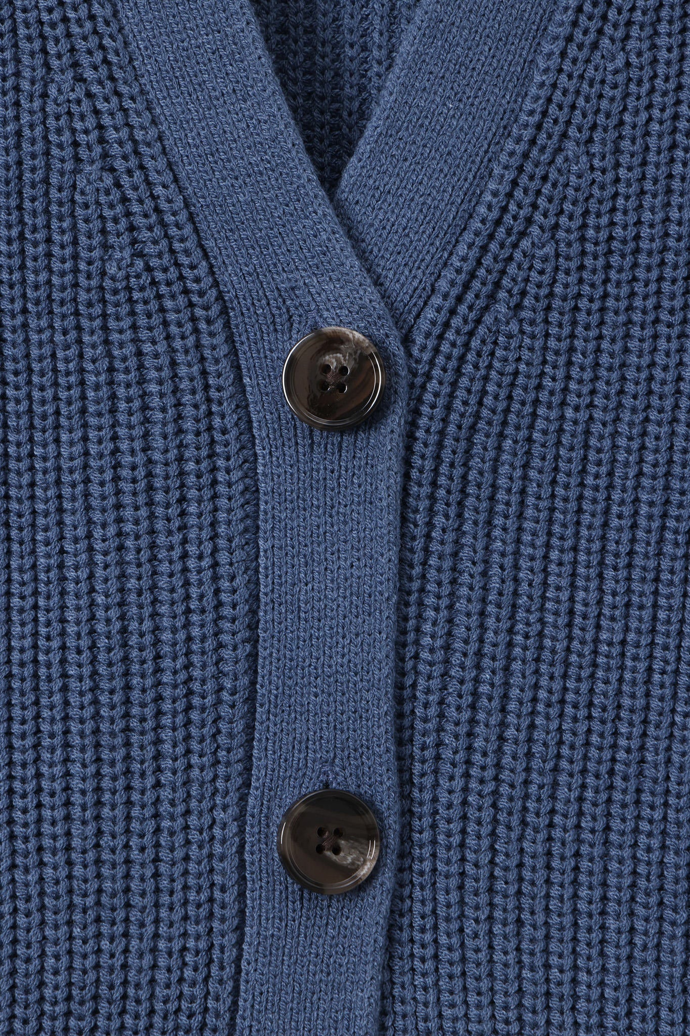 Close-up of a blue ribbed knit cardigan with dark brown buttons on a white background.