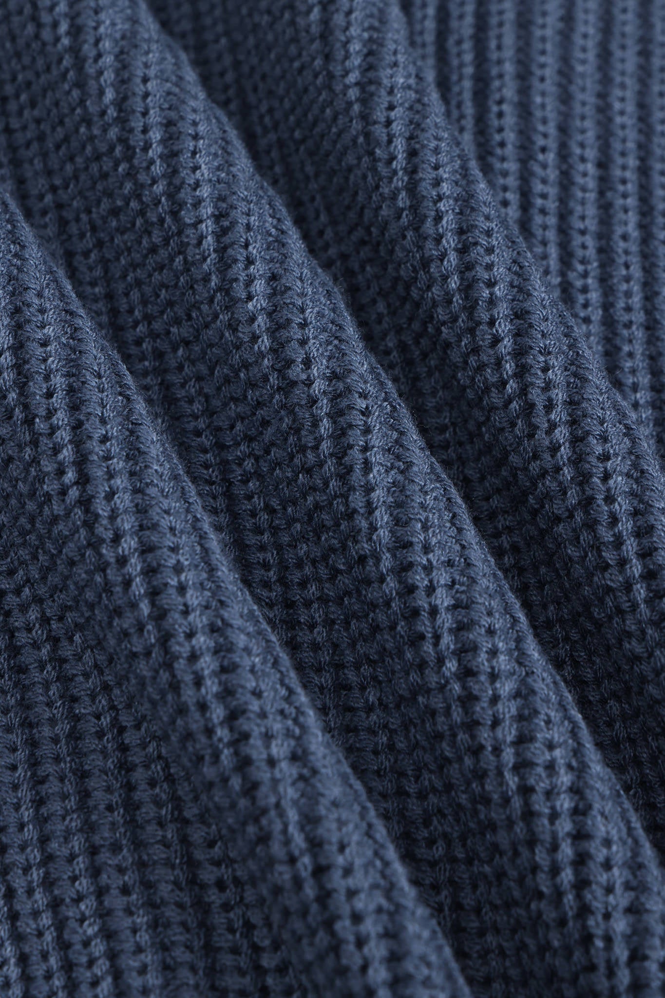 Close-up of a dark navy blue ribbed knit fabric texture with soft diagonal folds.
