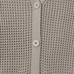 Close-up of a light taupe knit cardigan sweater showing the waffle-knit texture, V-neckline, and white buttons.