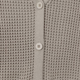 Close-up of a light taupe knit cardigan sweater showing the waffle-knit texture, V-neckline, and white buttons.