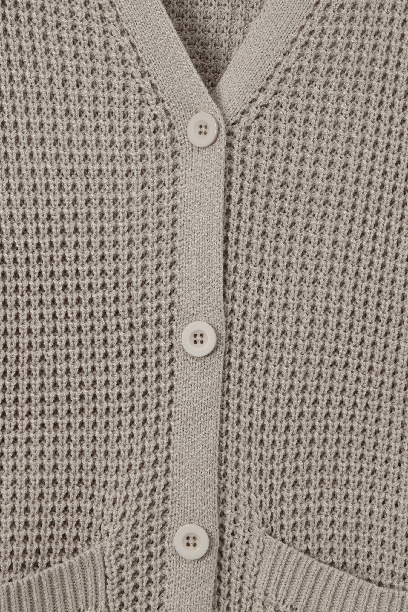 Close-up of a light taupe knit cardigan sweater showing the waffle-knit texture, V-neckline, and white buttons.