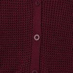 Close-up of a textured knit cardigan in deep burgundy with matching buttons, showing the ribbed collar, button placket, and pocket openings.