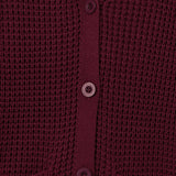 Close-up of a textured knit cardigan in deep burgundy with matching buttons, showing the ribbed collar, button placket, and pocket openings.