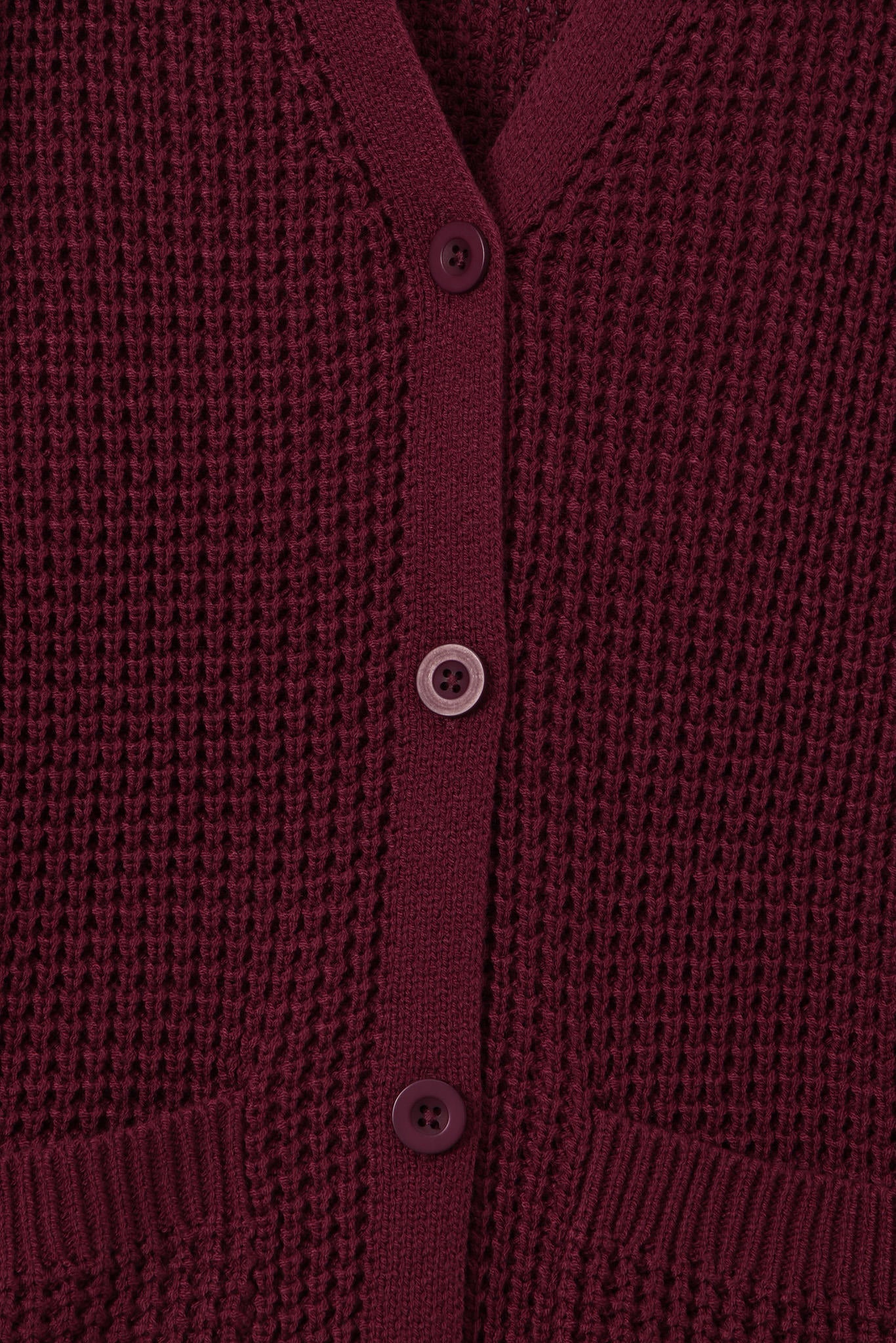 Close-up of a textured knit cardigan in deep burgundy with matching buttons, showing the ribbed collar, button placket, and pocket openings.