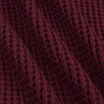 A close-up of a textured knit fabric in a deep burgundy or maroon color, showing the detailed waffle-knit pattern and soft folds.