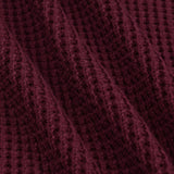 A close-up of a textured knit fabric in a deep burgundy or maroon color, showing the detailed waffle-knit pattern and soft folds.