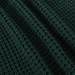 Close-up of a dark forest green waffle-knit fabric texture with soft folds.